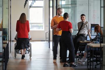 A group of young business people in a modern glass-walled office captures the essence of diversity and collaboration, while two colleagues, including an African American businessman in a wheelchair