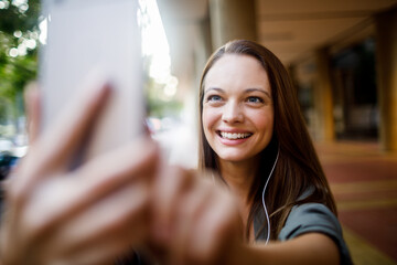 Young caucasian woman taking a picture with her smart phone while on a sidewalk in the city