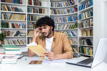 Young hispanic student upset studying inside university campus academic library, disappointed and...