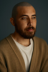 A dramatic portrait of a caucasian man with a shaved head and a brown beard wearing a cardigan.