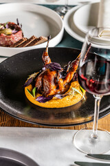 Quail in honey sauce with pumpkin porridge, served on a black plate in a restaurant.