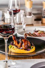 Quail in honey sauce with pumpkin porridge, served on a black plate in a restaurant.
