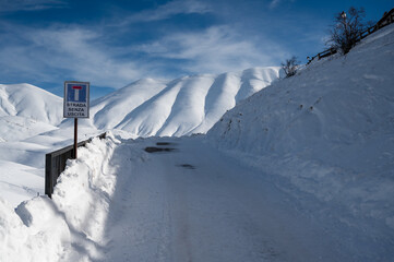 Winding mountain road with a sign at the side, blanketed in a layer of fresh snow