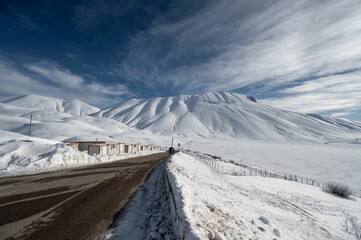 Winding road with majestic snow-capped mountains in the backdrop in Castelluccio di Norcia