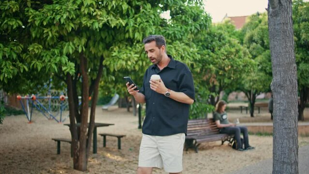 Italian freelancer video calling mobile phone walking greenery alley. Man call