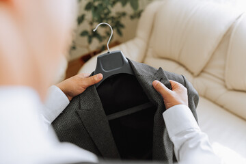 the man holds his black jacket on a hanger in his hands. The groom is preparing for the wedding...
