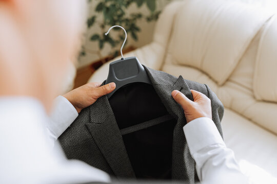 the man holds his black jacket on a hanger in his hands. The groom is preparing for the wedding ceremony. Detailed close-up photo of hands