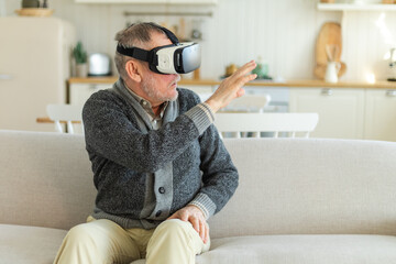 Excited mature senior man wearing using virtual reality metaverse VR glasses headset at home....