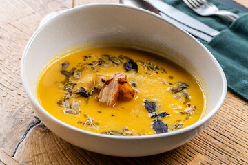 Spanish cuisine. Pumpkin soup with shrimp and pumpkin seeds, serving soup in a white plate in a restaurant.