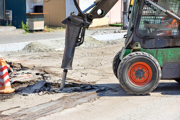The metal rod of a jackhammer on a construction tractor breaks up old asphalt at a construction site. - 635997244