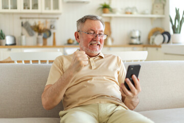 Middle aged senior man euphoric winner with smartphone. Older mature grandfather looking at cell...