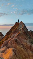 Fototapeta premium Vertical of a woman standing on a rocky mountaintop at sunset at Portugese coastline