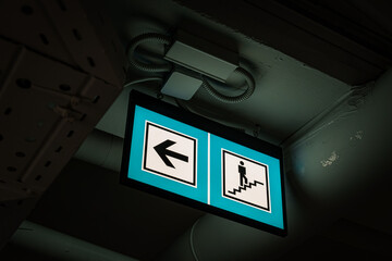 Naklejka premium Green And Blue Illuminated Directional Sign Leading To Staircase