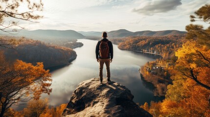A fictional man stands on top of a steep cliff overlooking a river and a forest.