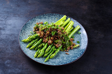 Green asparagus glazed with minced meet and herbs served as close-up on a design plate with text space
