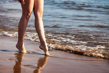 Crop photo of naked legs woman nudist walking on sea beach outdoors, close up. Foots of nude young...