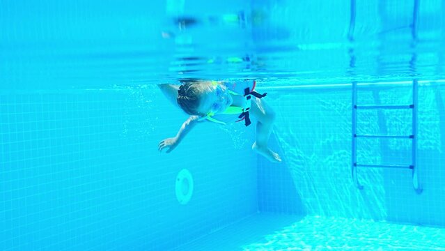 Portrait of little girl swimming underwater in goggles and vest in pool. Summer vacation