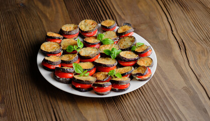 Fried eggplant on a white plate, garnished with basil leaves and tomatoes