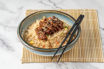 Overhead view of a bowl of cooked beef and rice with chopsticks