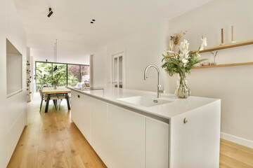 a kitchen and dining area in a house with wood flooring, white cabinets and an open door leading to the patio