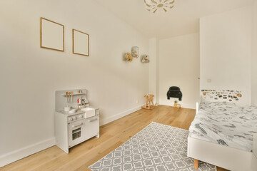 a child's room with white walls and hardwood flooring, including a grey patterned rug on the floor