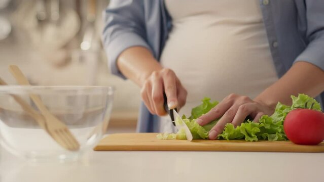 A kid, a young woman absorbed in the process, cuts a lettuce salad on a wooden table. Concept Parent-housewife cuts green lettuce salad with a knife uses different ingredients of vegetables, woman