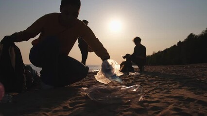 Earth day. Volunteers activists collects garbage cleaning of beach coastal zone. Woman and mans puts plastic trash in garbage bag on ocean shore. Environmental conservation coastal zone cleaning - Powered by Adobe