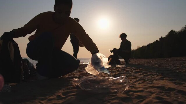 Earth day. Volunteers activists collects garbage cleaning of beach coastal zone. Woman and mans puts plastic trash in garbage bag on ocean shore. Environmental conservation coastal zone cleaning
