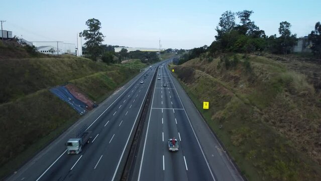 Drone footage of cars driving on lanes of highway road with trees and blue sky