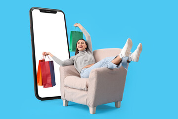 Happy woman with shopping bags sitting in armchair near big mobile phone on light blue background
