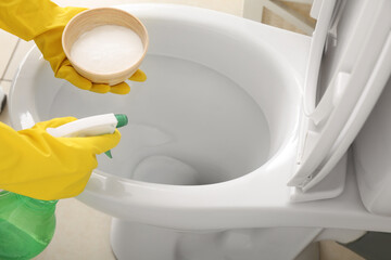 Woman in rubber gloves cleaning toilet bowl with baking soda and sprayer, closeup