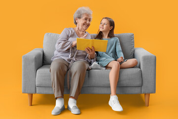 Little girl with her grandmother reading book on yellow background