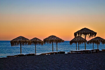 Umbrellas and parasols on the beach on Santorini island. Sunset on Greece.