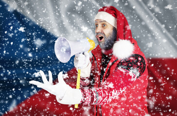 Santa Claus shouts into a megaphone and shows a hand gesture against the background of the flag of Czech Republic