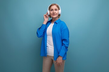 middle age business concept. mature woman listening to music with headphones on blue background copy space