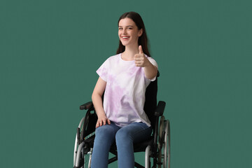 Obraz na płótnie Canvas Young woman in wheelchair showing thumb-up on green background