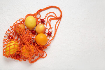 Mesh bag with fresh fruits on white background
