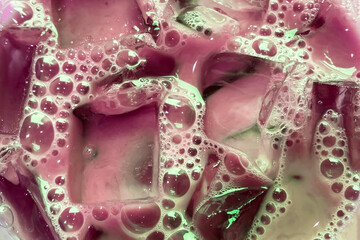 Colorful liquid with bubbles close up, texture of beverage with transparent ice cubes and bubbles