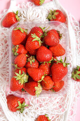 Mesh bag with fresh strawberry in plastic container on pink background, closeup
