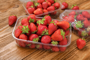 Plastic containers with fresh strawberry on wooden background, closeup