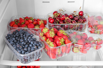 Plastic containers with fresh berries in refrigerator