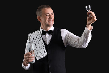 Mature waiter with glass and bottle of vodka on black background