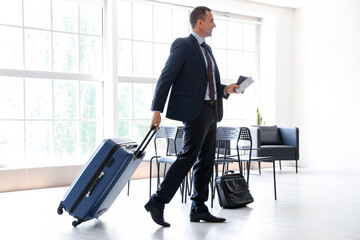 Mature businessman with suitcase walking in hall of airport