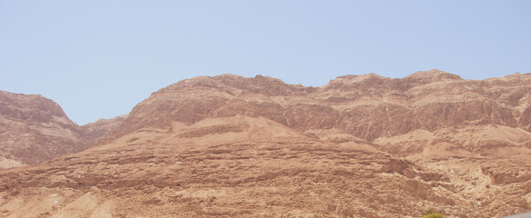 The desert landscape with a large sand cliff looks very large. the sand has a pink tint. And there is a fog of sand in the air.