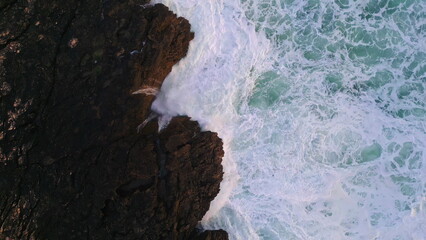 Powerful sea foaming splashing on dangerous rocks. Aerial rough ocean water.