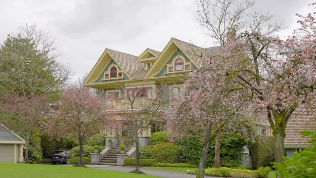 Establishing shot of two story stucco luxury house with garage door, big tree and nice spring blossom landscape in Vancouver, Canada, North America. Day time on Apr 2023. ProRes 422 HQ.