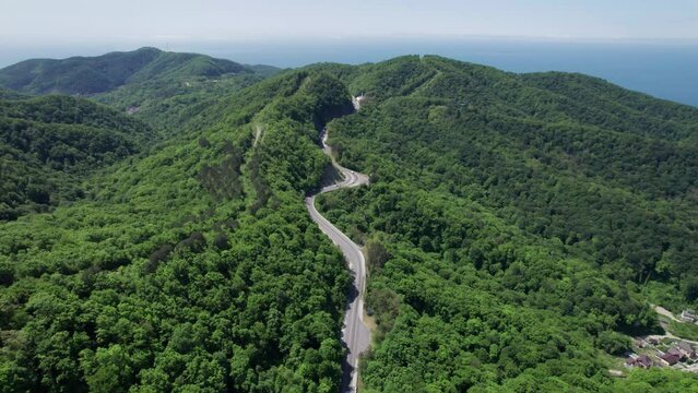 Aerial view of winding road from the high mountain pass. Great road trip trough the dense woods. Birds eye view.