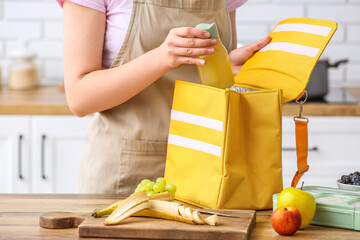 Woman packing bottle of juice into lunch box bag in kitchen