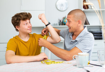 Father using measure tape for measuring girth of his son's biceps