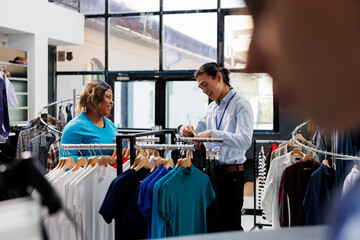 Shopaholic customer looking at new fashion collection, discussing clothes material in clothing store. African american woman shopping for formal wear, checking racks with stylish items